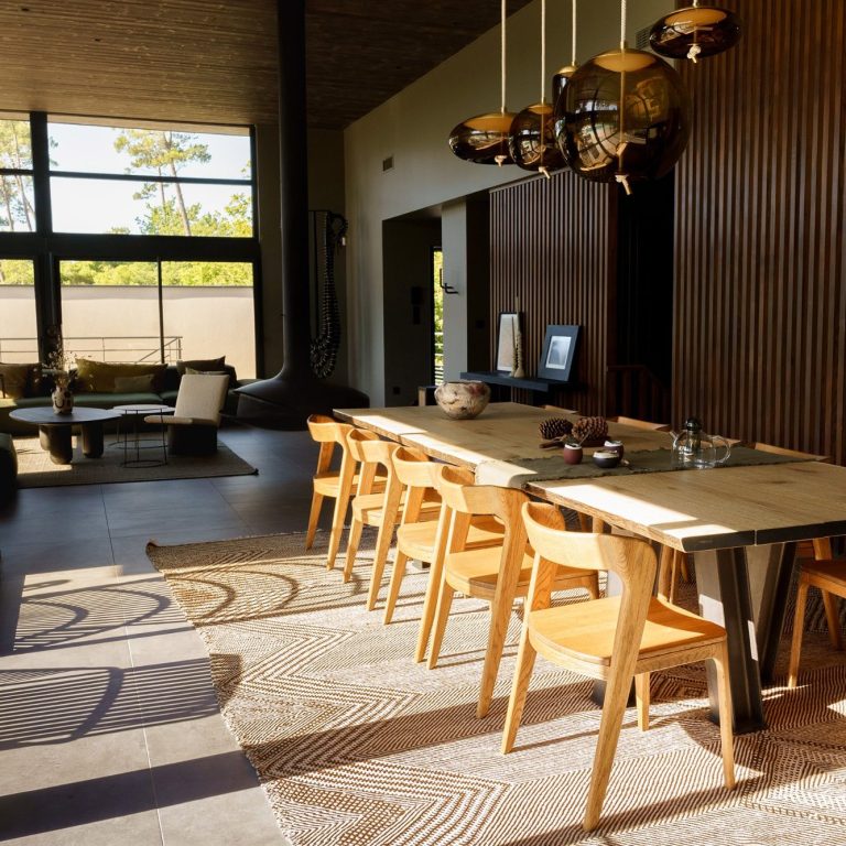 Salle à manger moderne avec une grande table en bois et des chaises, lumière naturelle abondante.