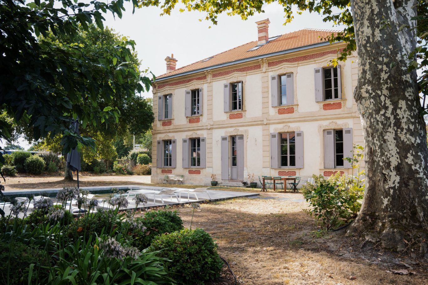 Belle maison traditionnelle avec jardin, arbres et allée pavée.